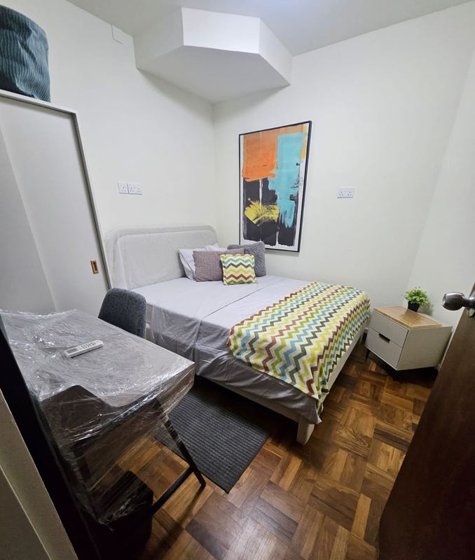 Common room with a bed, bedside drawers, study desk and chair, and parquet floor
